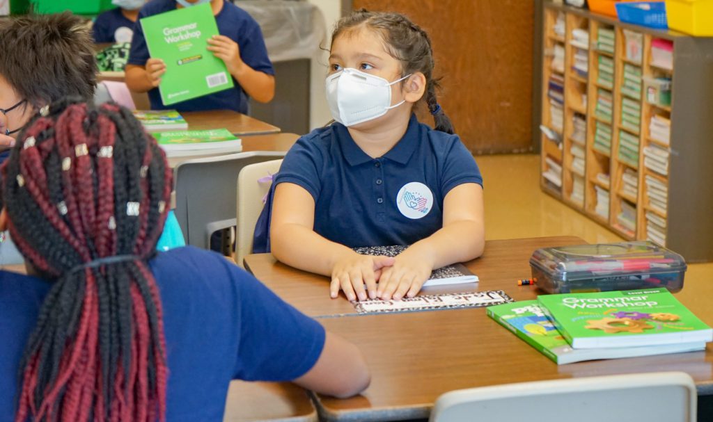 elementary student wearing mask sits at desk