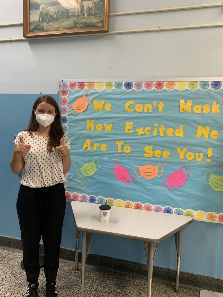 person gives two thumbs up in front of poster reading "we can't mask how excited we are to see you."