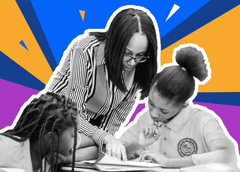 a woman pointing at a paper on a school desk in front of two female students.